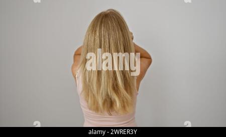 Blonde Frau von hinten vor weißem Hintergrund, mit ihrem langen Haar und ihrem rosa Oberteil. Stockfoto