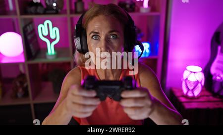 Reife Frauen spielen in einem neonbeleuchteten Raum bei Nacht fokussiert und tragen Kopfhörer Stockfoto