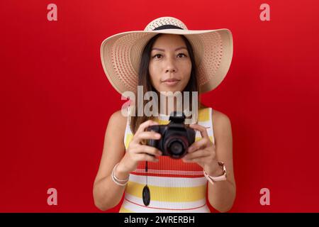 chinesin mittleren Alters mit Reflexkamera, Sommerhut entspannt mit ernstem Gesichtsausdruck. Einfaches und natürliches Betrachten der Kamera. Stockfoto