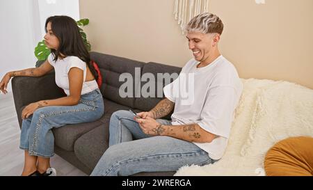 Ein Mann und eine Frau sitzen getrennt auf einem Sofa in einem modernen Wohnzimmer und zeigen Beziehungsdynamik mit einer neutralen Palette. Stockfoto