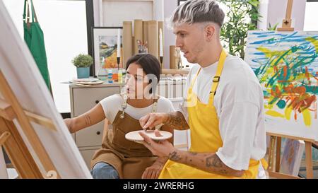 Ein Mann und eine Frau in Schürzen, die in einem Kunststudio an einem farbenfrohen abstrakten Gemälde arbeiten. Stockfoto
