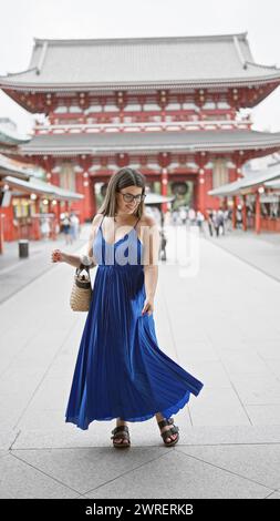 Die sprudelnde hispanische Frau tanzt fröhlich und dreht sich in wunderschönem Kleid inmitten der herrlichen Architektur des Senso-JI-Tempels in tokio. Sie ist durch japan gereist Stockfoto