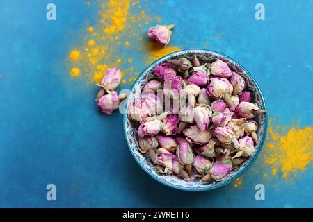 Getrocknete Rosenknospen aus nächster Nähe. Rosenblüten in einer blauen Keramikschale. Kräutertee-Zutat. Blauer Hintergrund mit Kopierraum. Stockfoto