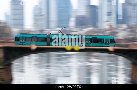 12. März 2024, Hessen, Frankfurt/Main: Eine Straßenbahn der Frankfurter Verkehrsgesellschaft (VGF) überquert den Main auf der Ignatz-Bubis-Brücke (Schuss mit langsamerer Verschlusszeit und Zuggeschwindigkeit). Nach den Zugführern und dem Kabinenpersonal bei Lufthansa streiken ab Mittwoch die Mitarbeiter des öffentlichen Verkehrs. Foto: Arne Dedert/dpa Stockfoto