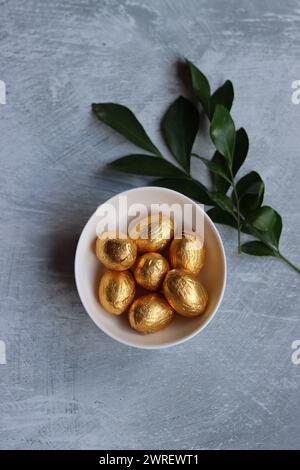 Schokoladen-Ostereier in Goldfolie gewickelt. Weiße Frühlingsblumen und Süßigkeiten von Ester von oben. Strahlendes Stillleben im Frühling. Stockfoto