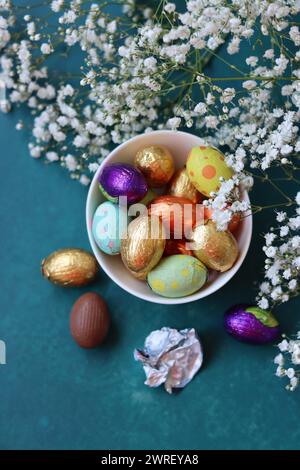 Eiern aus Osterschokolade mit Folie in eine Glasschale gewickelt. Osterfest-Konzept. Buntes Stillleben mit Süßigkeiten. Texturierter Hintergrund mit Kopierraum. Stockfoto