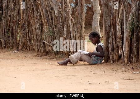 OMO VALLEY, ÄTHIOPIEN – 24. NOVEMBER 2011: Außenporträt eines nicht identifizierten jungen afrikanischen Mädchens, das am 24. November 2011 in Omo Valley ein Buch liest Stockfoto