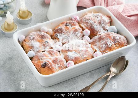 Ostern heiße Kreuzbrötchen. Traditionelle Osterspezialitäten sind Kreuzbrötchen mit Rosinen, Butter, Schokoladeneiern mit blühenden Kirschen oder Apfelblüten auf Rost Stockfoto