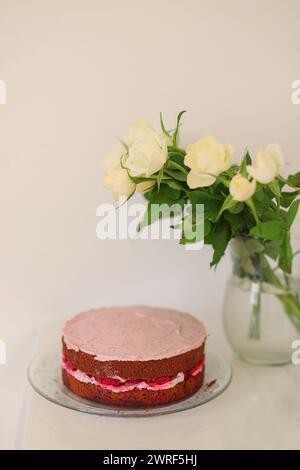 Hausgemachter Kuchen mit rosa Creme und einem Strauß weißer Rosen in einer Vase Stockfoto