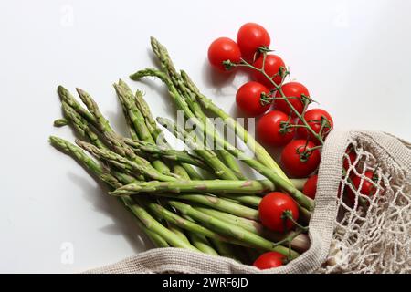 Frische Kirschtomaten und grüner roher Spargel auf weißem Hintergrund mit Kopierraum. Fresh-Konzept. Zutaten für vegetarische Gerichte. Stockfoto