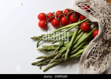 Frische Kirschtomaten und grüner roher Spargel auf weißem Hintergrund mit Kopierraum. Fresh-Konzept. Zutaten für vegetarische Gerichte. Stockfoto
