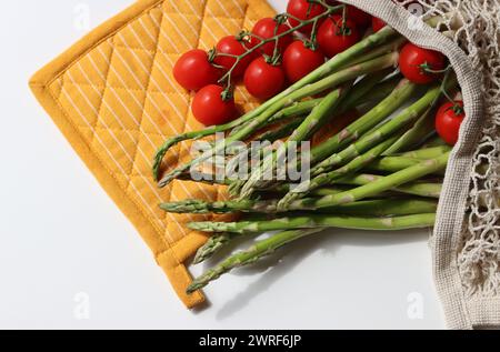 Frische Kirschtomaten und grüner roher Spargel auf weißem Hintergrund mit Kopierraum. Fresh-Konzept. Zutaten für vegetarische Gerichte. Stockfoto