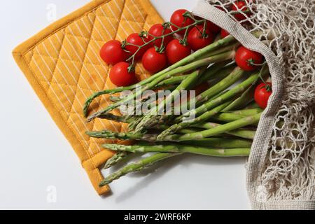 Frische Kirschtomaten und grüner roher Spargel auf weißem Hintergrund mit Kopierraum. Fresh-Konzept. Zutaten für vegetarische Gerichte. Stockfoto