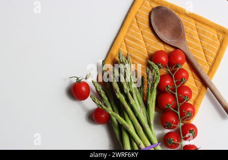 Frische Kirschtomaten und grüner roher Spargel auf weißem Hintergrund mit Kopierraum. Fresh-Konzept. Zutaten für vegetarische Gerichte. Stockfoto