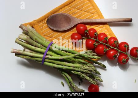 Frische Kirschtomaten und grüner roher Spargel auf weißem Hintergrund mit Kopierraum. Fresh-Konzept. Zutaten für vegetarische Gerichte. Stockfoto