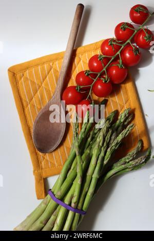 Frische Kirschtomaten und grüner roher Spargel auf weißem Hintergrund mit Kopierraum. Fresh-Konzept. Zutaten für vegetarische Gerichte. Stockfoto