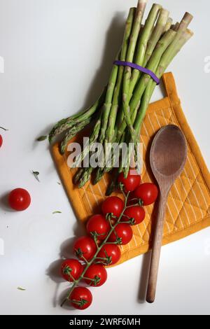 Frische Kirschtomaten und grüner roher Spargel auf weißem Hintergrund mit Kopierraum. Fresh-Konzept. Zutaten für vegetarische Gerichte. Stockfoto