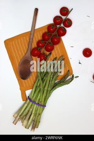 Frische Kirschtomaten und grüner roher Spargel auf weißem Hintergrund mit Kopierraum. Fresh-Konzept. Zutaten für vegetarische Gerichte. Stockfoto