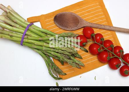 Frische Kirschtomaten und grüner roher Spargel auf weißem Hintergrund mit Kopierraum. Fresh-Konzept. Zutaten für vegetarische Gerichte. Stockfoto