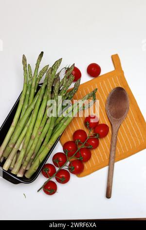 Frische Kirschtomaten und grüner roher Spargel auf weißem Hintergrund mit Kopierraum. Fresh-Konzept. Zutaten für vegetarische Gerichte. Stockfoto