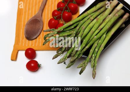 Frische Kirschtomaten und grüner roher Spargel auf weißem Hintergrund mit Kopierraum. Fresh-Konzept. Zutaten für vegetarische Gerichte. Stockfoto
