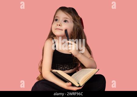 Bild auf rosafarbenem Hintergrund mit einem sehr schönen und molligen kleinen Mädchen, das kleine Mädchen liest gerne Bücher und ist mollig und denkt, während es hält Stockfoto