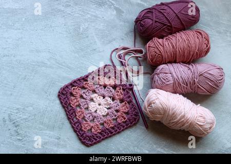 Das Häkelmuster des Granny-Vierecks. Farbenfrohes Foto von weichem rosa Bio-Garn. Hobbys und Freizeitkonzept. Hellgrauer Hintergrund mit Kopierraum. Stockfoto