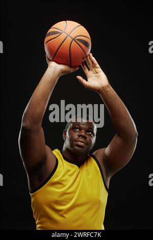 Vertikales Porträt eines afroamerikanischen Basketballspielers, der den Ball vor schwarzem Hintergrund vorbeiführt Stockfoto