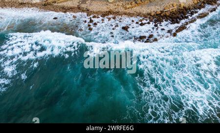 Eine kräftige dunkelblaue Welle mit weißem Schaum, die auf das felsige Ufer stürzt. Ein Blick von der Atlantikseite aus der Vogelperspektive. Piélagos, Kantabrien, Spanien. Stockfoto