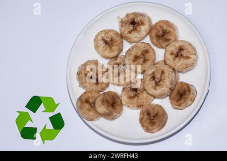 Ein Teller mit Bananenscheiben und Chips, die schwarz sind, das heißt, sie sind fast verdorben, sie stehen auf einem weißen Hintergrund, als Zeichen dafür Stockfoto