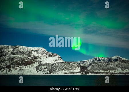 Spektakuläre Schauplätze intensiver Nordlichter oder Aurora Borealis, die grüne Wirbel über verschneiten Bergen in Nordnorwegen bilden Stockfoto