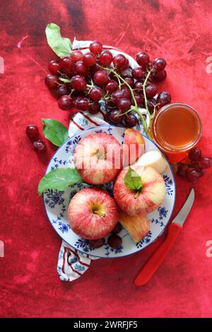 Rote Äpfel und Trauben auf rotem Hintergrund mit einer Tasse Honig. Jüdisches Neujahrsfest Rosch Hashana. Stillleben mit saisonalem Obst und Honig. Stockfoto