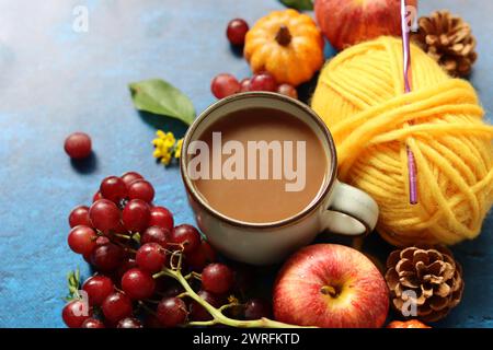 Tasse Kaffee mit Milch, Waffeln, Äpfeln und Schokolade und Garnbällchen auf blauem Hintergrund mit Kopierraum. Gemütliches Herbstkonzept. Stockfoto