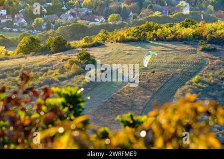 Gleitschirmfliegen über eine malerische Herbstlandschaft mit bunten Bäumen und einem Wohngebiet im Hintergrund Stockfoto