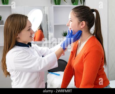 Pflanzenkosmetologe in weißen Handschuhen, die die Gesichtshaut junger Klientin vor Schönheitsverfahren im Salon untersucht. Hochwertige Fotos Stockfoto