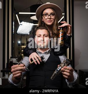 Friseur Mann und Mädchen halten Werkzeuge mit Friseureigenschaften, die auf einem Stuhl im Salon sitzen. Stockfoto