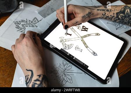 Horizontales Foto die Hand eines Künstlers rendert sorgfältig ein Tattoo-Design auf einem Grafiktablett inmitten von Papierskizzen. Konzeptgeschäft, Kunst. Stockfoto