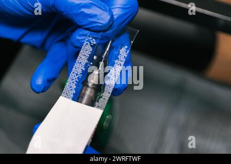 Horizontales Foto Nahaufnahme der Hände eines Tätowierers in blauen Handschuhen, vorsichtig eine Tätowiermaschine mit einer frischen Nadel für den Gebrauch vorbereiten. Kopierbereich. Stockfoto