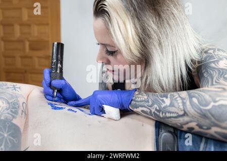 Horizontales Foto ein Bild, das die intensive Hingabe einer Tätowiererin feststellt, während sie ein Tattoo akribisch einfärbt, ihr eigener Körper ist eine Leinwand ihres Handwerks. C Stockfoto