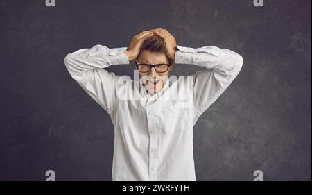 Unglücklicher depressiver junger Mann steht auf grauem Hintergrund und schreit mit dem Kopf. Stockfoto