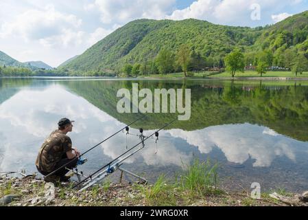 Angelabenteuer, Karpfenfischen auf dem See. Mann, der neben Angelruten hockt und darauf wartet, einen Fisch zu fangen. Rutenkapsel mit Angelruten und Beißalarmen Stockfoto