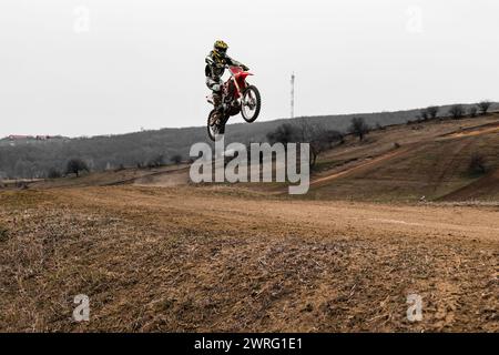 Eine Person schwebt mit einem Motocross-Dirt-Bike durch den Himmel, trägt einen Helm, während Reifen und Rad des Fahrzeugs Schmutz aufwirbeln. Das Motorrad ist ein Stockfoto