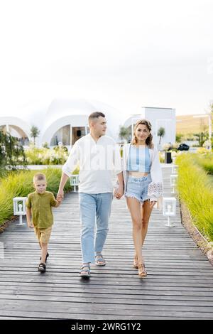 Mann und Frau gehen mit ihrem Sohn einen Holzsteg hinunter, umgeben von Bäumen und Natur. Sie schlendern gemütlich den Weg entlang. Stockfoto