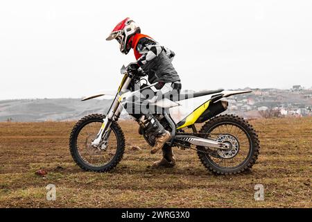 Ein Motorradrennfahrer mit Helm fährt auf einer Feldstraße unter dem Himmel auf einem mit Autoreifen und Rädern ausgestatteten Dirt Bike Stockfoto