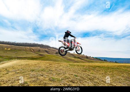 Eine Person fährt auf einem Motorrad auf einer Feldstraße mit einem Motocross-Helm. Der Reifen wirft während der Fahrt Staub in den Himmel Stockfoto