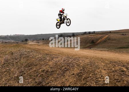 Eine Person schwebt mit einem Motocross-Dirt-Bike durch den Himmel, trägt einen Helm und holt etwas Luft auf das Rad und den Reifen des Fahrzeugs Stockfoto