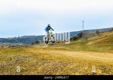 Eine Person reißt auf einem Motocross-Bike eine unbefestigte Straße auf, trägt einen Helm und schleudert Staub auf, während sie durch das raue Gelände unter freiem Himmel navigiert Stockfoto