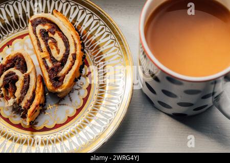 Kleicha, irakische Dattelkekse in Spiralform mit nigella-Samen auf kunstvoll verziertem Goldmuster, Tasse Tee, Kaffee mit Sahne Stockfoto