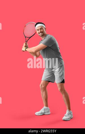 Sportlicher junger Mann, der Tennis auf rotem Hintergrund spielt Stockfoto