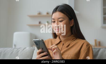 Asiatisch chinesisch koreanisch Geschäftsfrau Frau Mädchen Freiberufler Arbeit von zu Hause in der Küche lesen gute Nachrichten lächelnd Handy benutzen Waren im Internet wählen Stockfoto